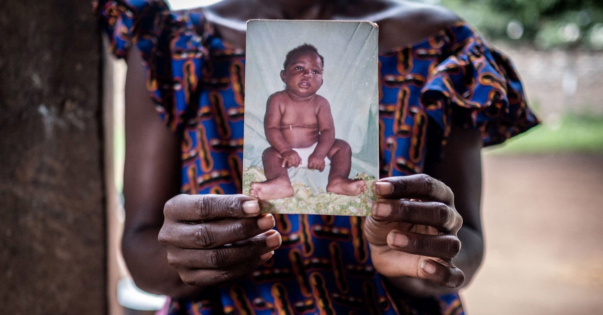 An African woman holds a worn photo of an infant in her hands.