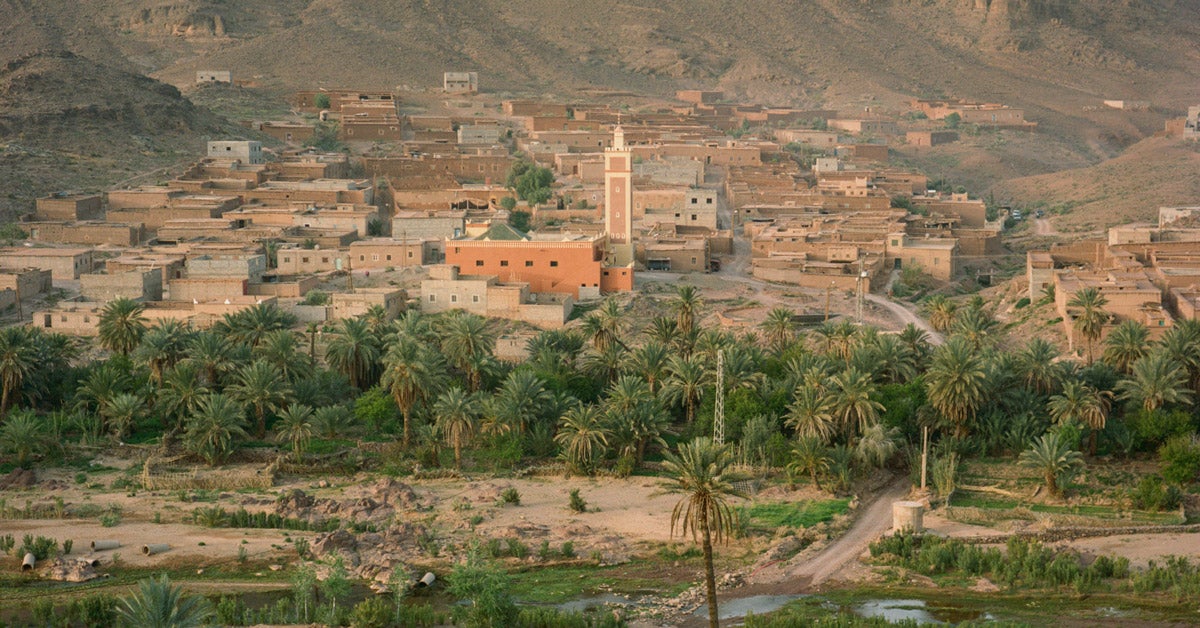 Aerial photo of the Fint Oasis in southern Morocco: green palm trees, a small water source and clay buildings stand among dry hills and dirt roads.
