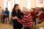 A woman dances with an elderly male resident during a concert at a community room. Other spectators sit and watch and record with their cell phones.