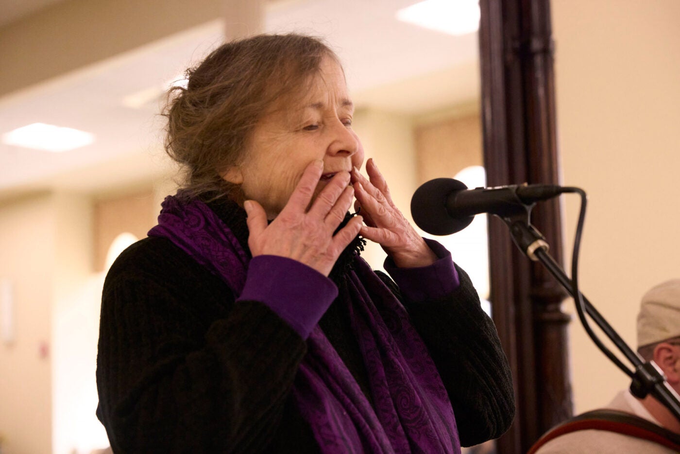 A woman expressively sings with her hands touching her lips.