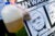 A protestor holds a gallon of murky tap water, a bag of hair, and a sign with two mug shots sketches of Rick Snyder.