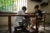 An intern at a Cambodian prosthetics clinic checks the leg and prosthetic of a 14 y/o boy. The boy sits in a wooden chair near a walking board with railings.