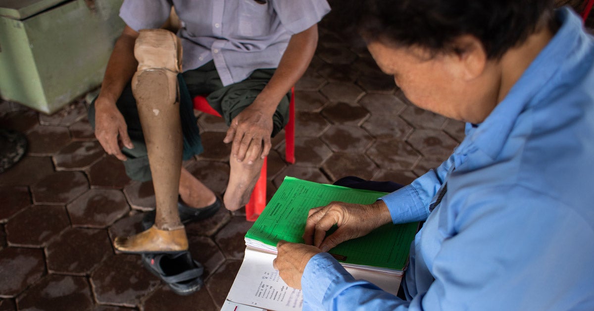 A prosthetics patient with a missing leg limb gets his chart reviewed and leg cared for a by a community health care worker near his home in Cambodia.
