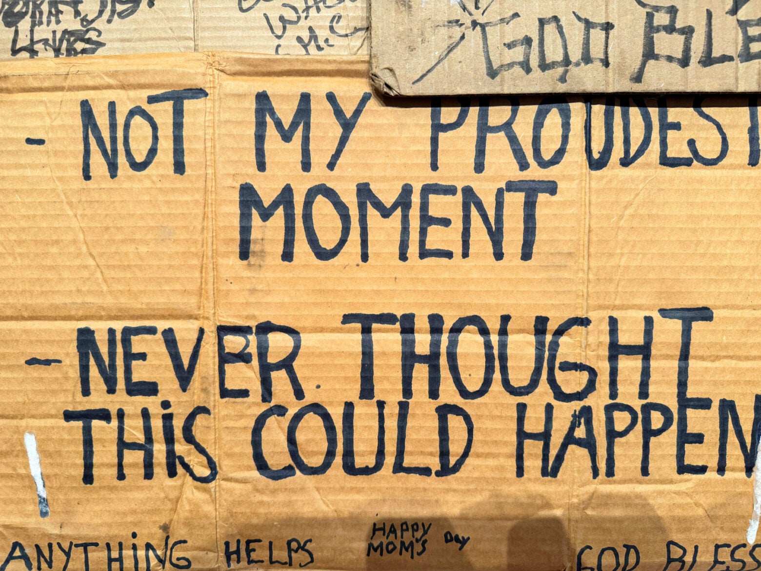 Close-up of a cardboard sign with handwritten text reading: "not my proudest moment. Never thought this could happen."
