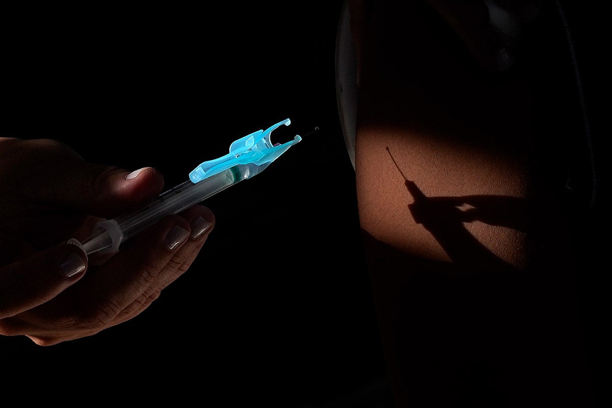 The shadow of a syringe is cast on the arm of a person receiving a vaccine.