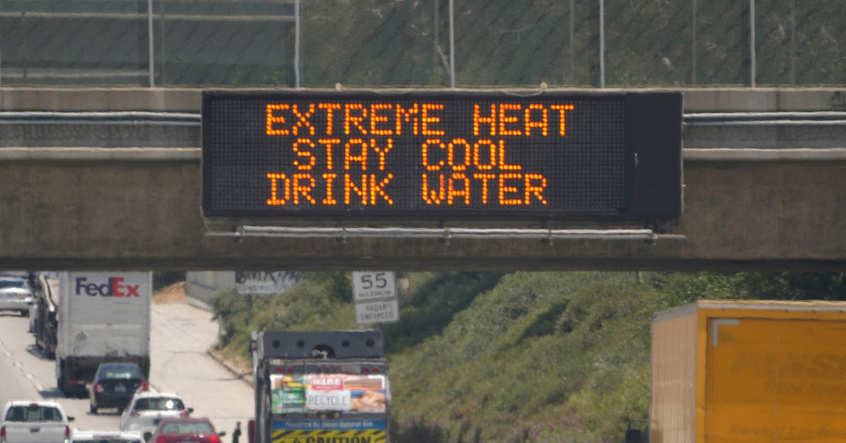 An “Extreme Heat, Stay Cool, Drink Water” digital highway sign above a busy interstate.