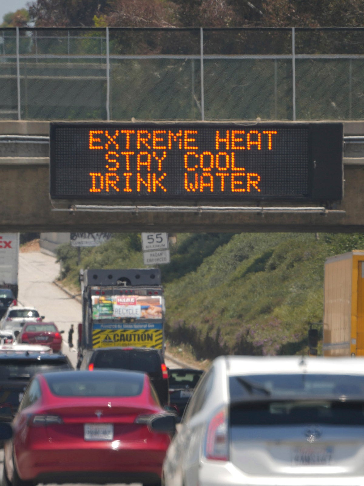 An “Extreme Heat, Stay Cool, Drink Water” digital highway sign above a busy interstate.