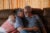 Scott and Abby Tennant embrace on a brown couch in their home.