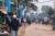 A busy street in Kibera, Kenya. Blue pillars holding blue water pipes line the street and hang above.