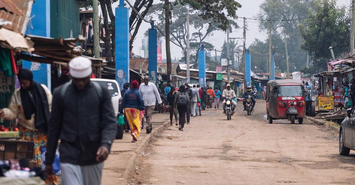 A busy street in Kibera, Kenya. Blue pillars holding blue water pipes line the street and hang above.