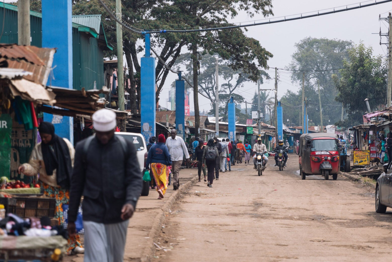 A busy street in Kibera, Kenya. Blue pillars holding blue water pipes line the street and hang above.