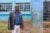 Samuel Onyango stands in a dirt school yard next to a blue pillar that supports the new installed water system.