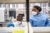 Two African medical researchers in a lab look at a medical device. Both wear protective masks and PPE.