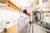 Christian Happi wearing an embroidered white lab-coat enters a dry lab through a set of clear double-doors at ACEGID.