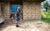 Oladipo Eniayewu wears bright, patterned clothing, and stands with a cane beside his son's grade behind a stone-brick building near a grassy field near Owo, NIgeria.