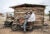 Michael Olonite sits on his motorcyle with Jimoh Tajudeen on the back. They are in front of a wood hut in Nigeria.