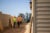 Construction workers dressed in bright green and orange outfits look at an apartment building. Only a small part of the building's siding and roof is visible from the right side of the frame.