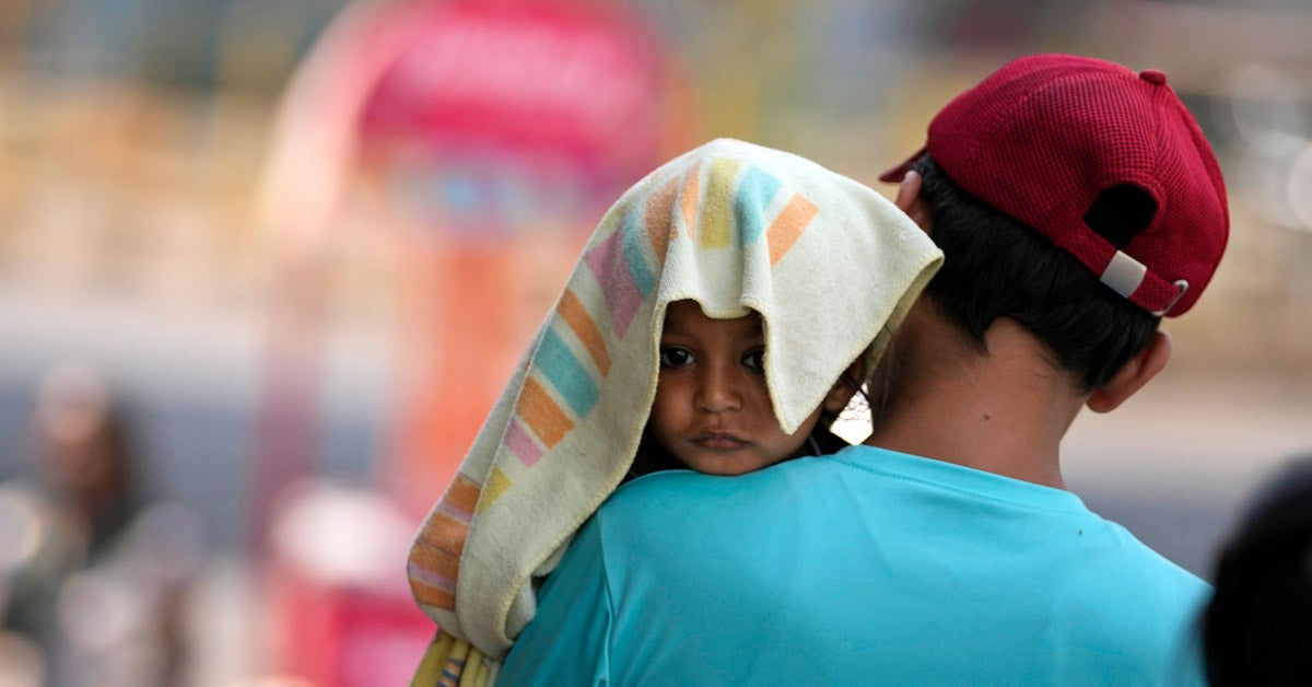 A man with his back to the camera carries a child, head covered with a towel to protect from the heat, in Jammu, India.