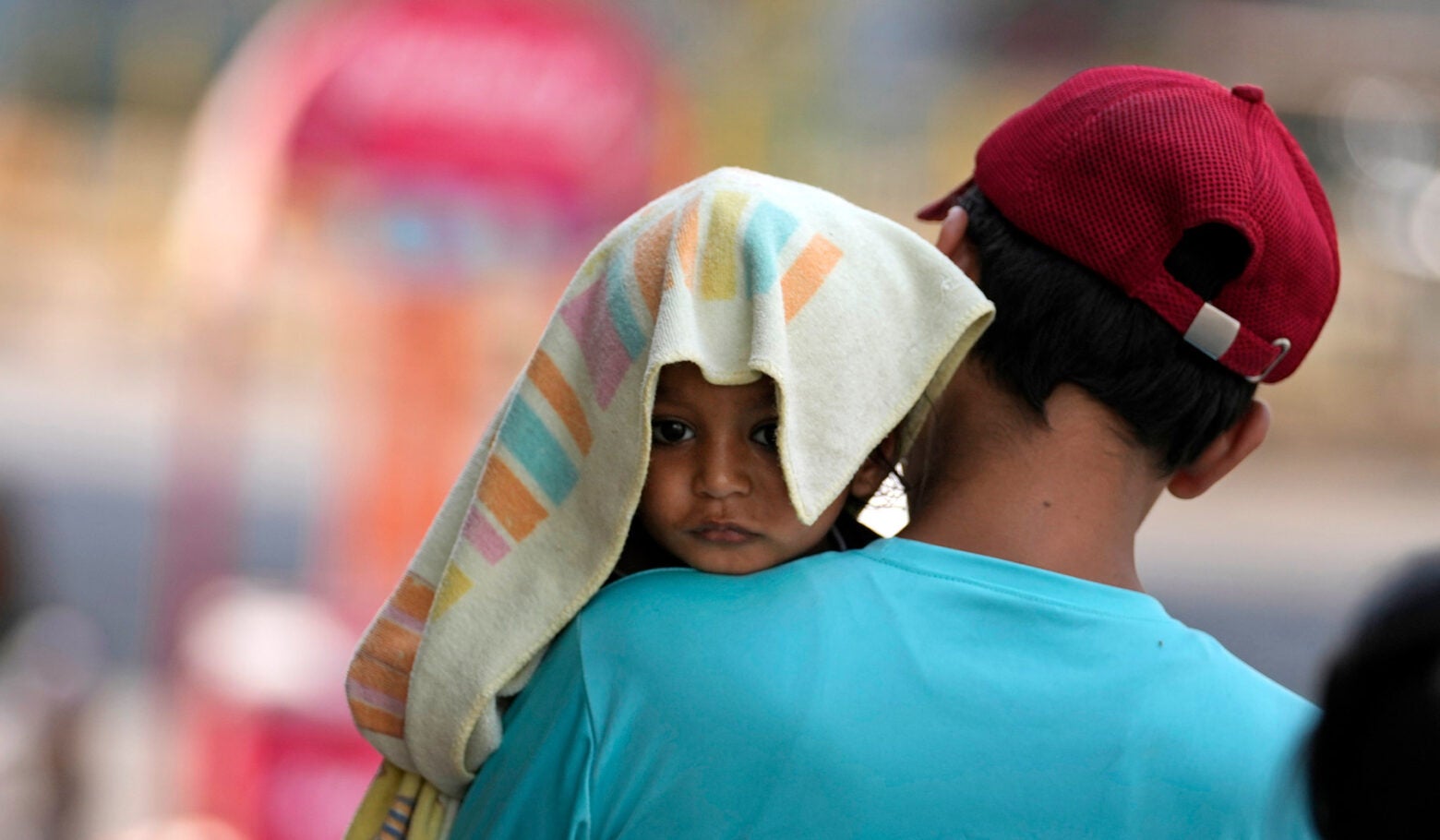 A man with his back to the camera carries a child, head covered with a towel to protect from the heat, in Jammu, India.