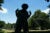 A teen stands in the middle of a grassy rec field and makes the "rock on" signs with his hands. His body is in silhouette.