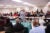 A trainer specializing in community violence intervention speaks to a classroom full of professionals working in the field of violence intervention. Students sit at long tables arranged in rows.