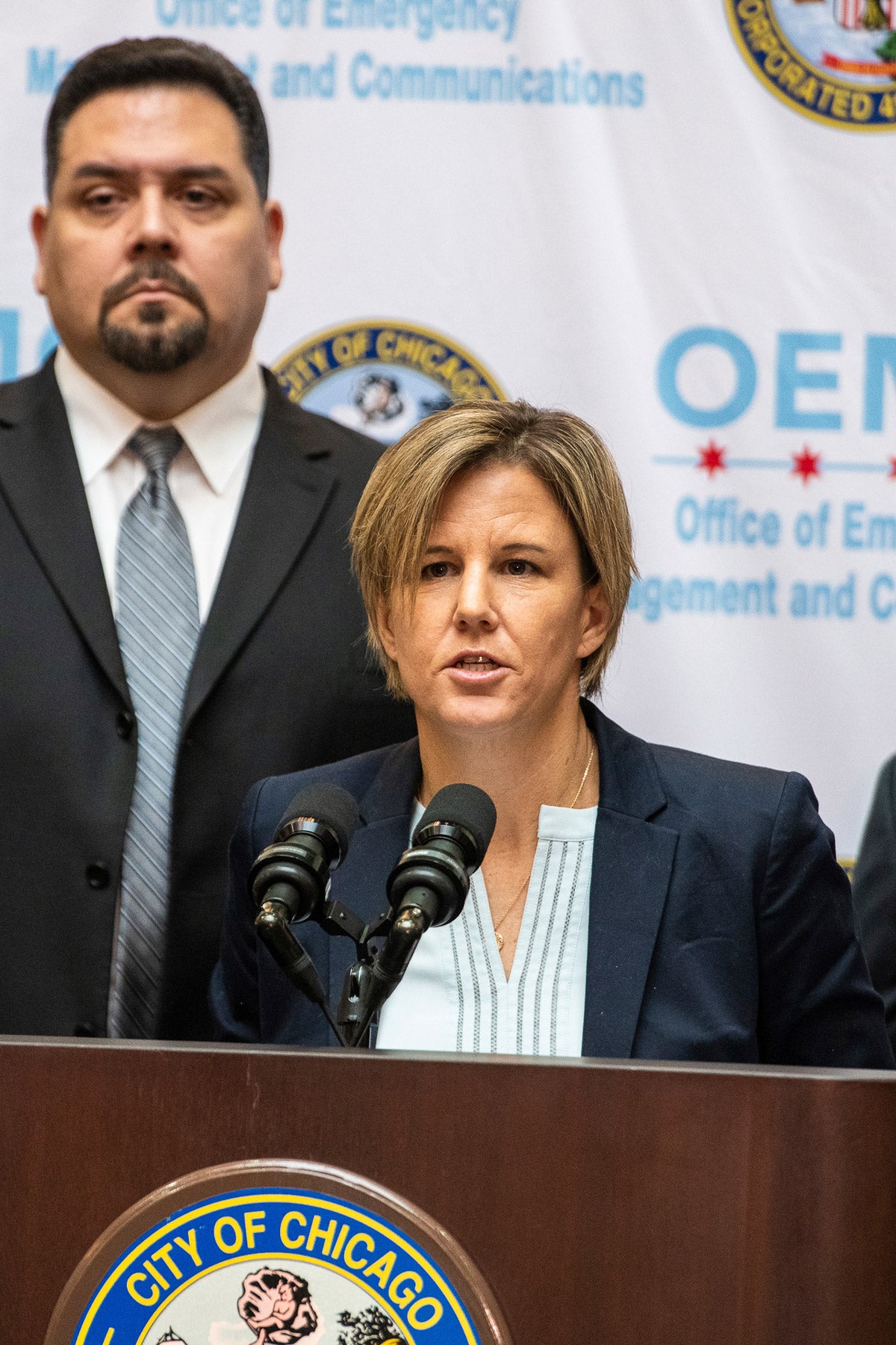 Jennifer Layden speaks into two microphones at podium at a city of Chicago press conference.