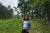 Bonita Green stands in the middle of a partially cleared wooded area outside of Durham, North Carolina. She wears dark jeans, a jean jacket a grey t-shirt and glasses. She looks directly at the camera.