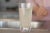 A glass of dirty water stands on a kitchen counter near a sink. A blurred person in a pink shirt is in the background