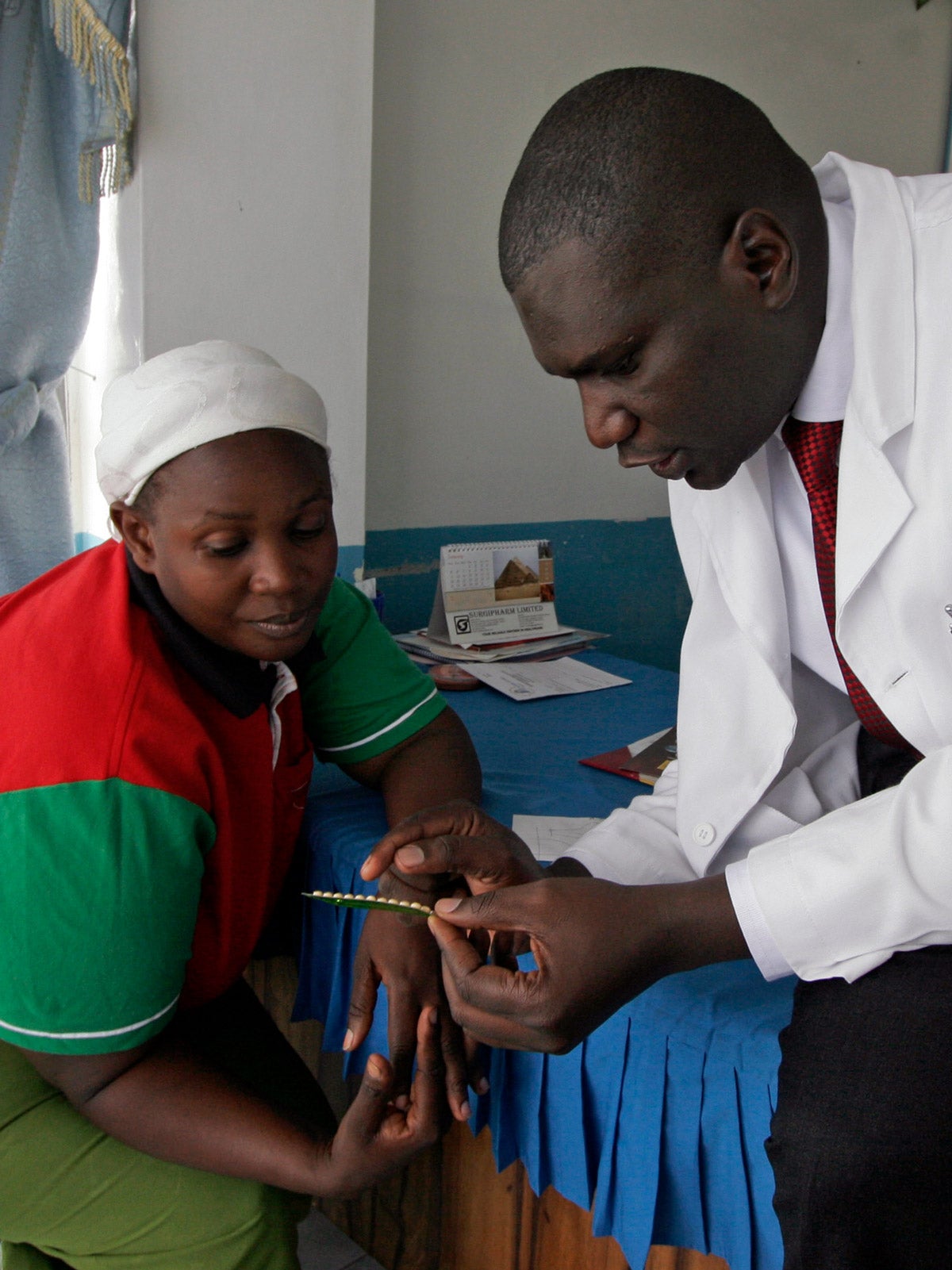 A male Kenyan doctor show a birth control packet to a female patient at a clinic in Nairobi.