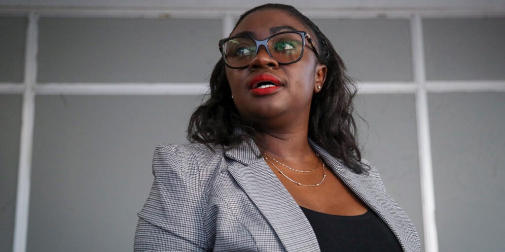 Kenyan senator Gloria Orwoba speaks at a press conference. She wears a grey striped blazer, glasses and red lipstick.