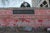 Two nurses in dark teal scrubs and masks sit on top of The National COVID Memorial Wall in London. The wall is covered with handrawn red hearts and messages.