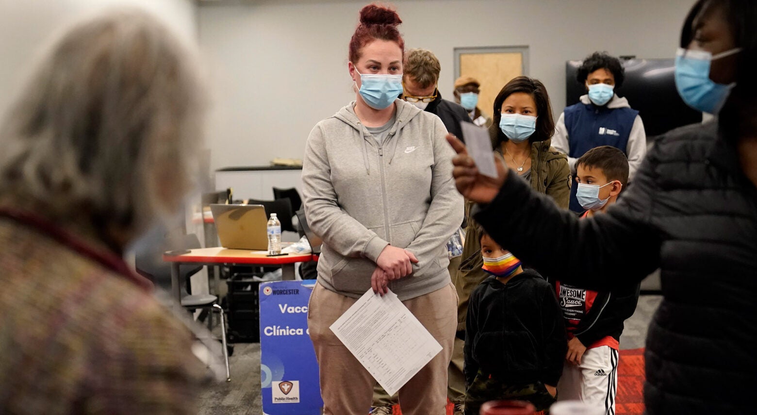 A line of people wearing mask a mobile vaccine clinic.