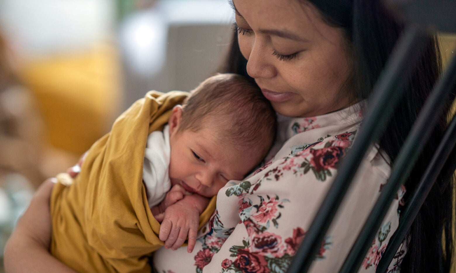 Mom rocking her infant who's wrapped in a yellow blanket.