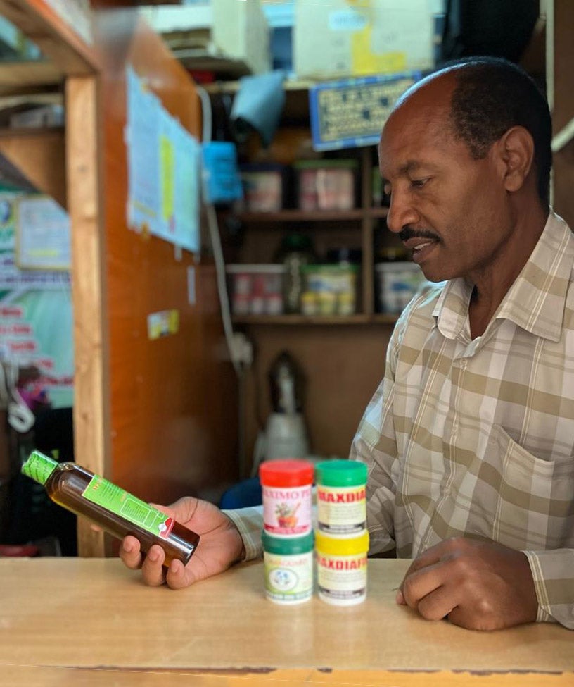 Moses Muthom, a Kenya herbalist, looks at a bottle of medicine in his hand while standing behind counter.